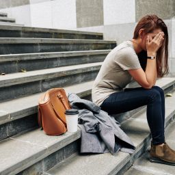 Pretty young woman sitting on steps outdoor and covering face when crying after difficult break up